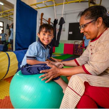 A woman plays with a child who is sitting on a large ball