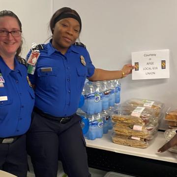 Three TSA agents standing by tables filled with water and food