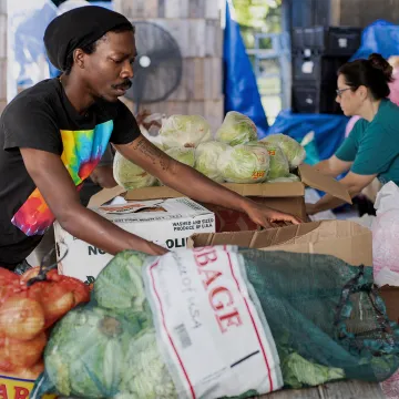 People peruse onions, cabbages and other vegetables at a farmer's market. 