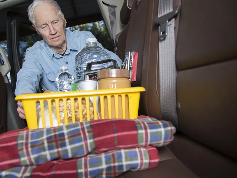 Man placing a bin of disaster preparation items into the backseat of a car